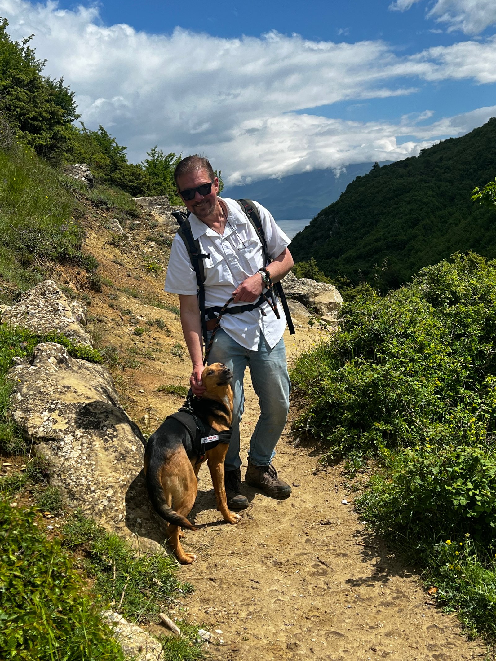 Dog hiking with owner on a dramatic mountain trail in Albania with a wide valley below